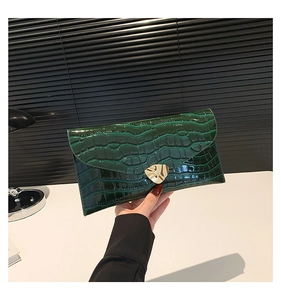 Détail d'une pochette enveloppe vert foncé à texture crocodile et fermoir doré chic