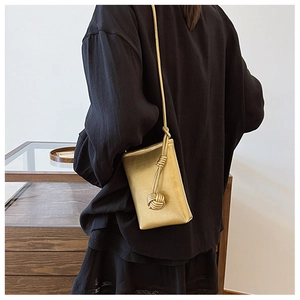 Chic gold metallic crossbody phone bag with decorative knotted shoulder strap on model