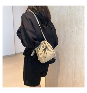 Close-up of minimalist beige drawstring bucket bag worn on shoulder by a model