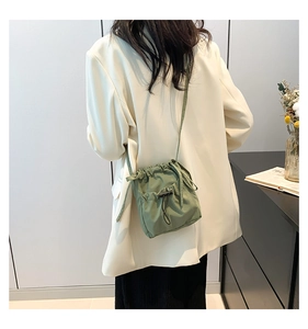 Detail of light green drawstring crossbody bucket bag worn on shoulder by model