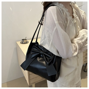 Detail of a black faux leather shoulder bag featuring a large decorative bow and strap