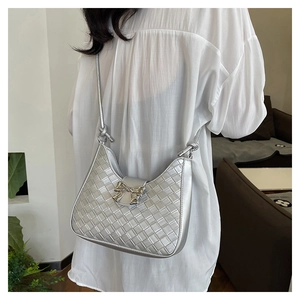 Detail view of woven silver underarm bag with decorative metal bow buckle and slim straps