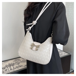 Detail of white woven crescent bag featuring a silver bow buckle and knotted shoulder strap