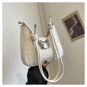 Detail view of a white woven leather handbag with a silver metallic bow and drawstring handles