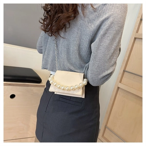 Detailed shot of beige mini bag with oversized pearl handle and metallic chain strap