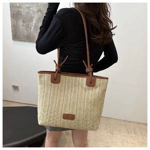 Detalle de bolso tote de paja tejida con asas de cuero marrón y detalles de nudos