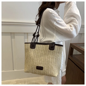 Detalle de bolso tote de paja tejida con ribete de cuero marrón llevado por una modelo