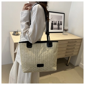 Detalle del bolso tote de paja tejida con correas de cuero negro y textura vertical