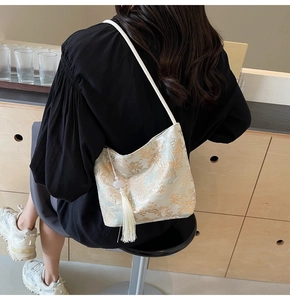 Detail of jacquard shoulder bag with tassel and jade-like bead on white fabric