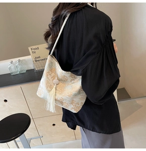 Details der cremefarbenen Beuteltasche mit Goldmuster und eleganter weißer Quaste