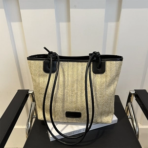 Bolso tote de paja tejida beige con correas finas de cuero negro sobre libro blanco