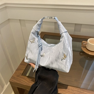 Light blue ruched handbag with silver butterfly accents on a glass table setup