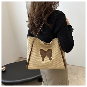 Detail of woven straw tote bag with brown butterfly patch and leather shoulder straps