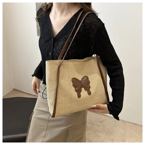 Detail of a large straw tote bag featuring leather handles and a butterfly patch