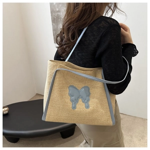Detail of hand-woven straw tote bag with blue butterfly patch and leather shoulder straps