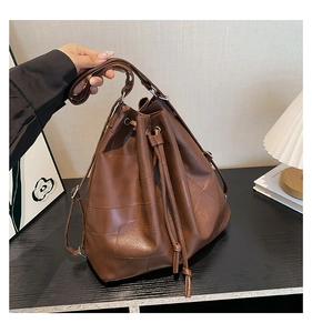 Detail of a brown leather drawstring bucket bag with geometric patchwork and stitching