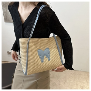 Detail of woven straw tote bag featuring light blue butterfly appliqué and shoulder straps