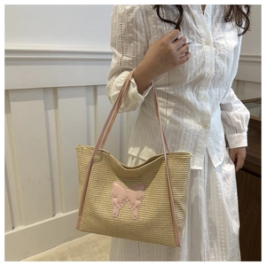 Close-up of a beige straw tote bag with pink butterfly patches and straps on a model