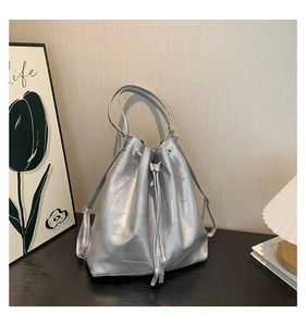 Detail of silver textured bucket bag with drawstring closure on dark wooden table