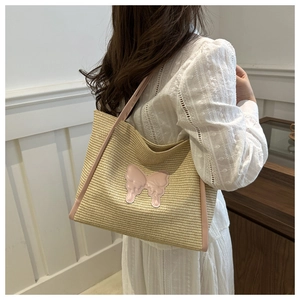 Close-up of woven straw tote bag featuring a pink butterfly patch and fine straw texture