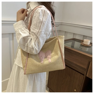 Large beige straw tote bag with pink bow detail and PU leather handles on a model