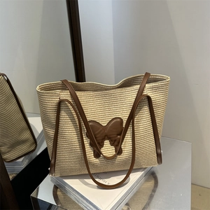 Large beige woven straw tote bag with brown butterfly leather patch and long handles