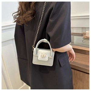 Detail of silver micro crossbody bag featuring a white butterfly buckle and gold chain