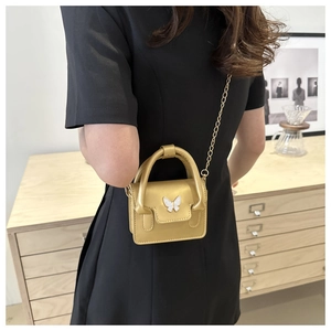 Detail of a gold mini crossbody bag with a white butterfly metal buckle and chain strap