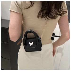 Detail of black mini crossbody bag with white butterfly and gold chain on model