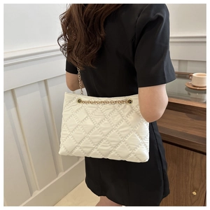 Rear view of white quilted tote bag with gold chain strap worn by a female model