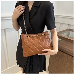 Brown quilted tote bag with golden chain strap worn by a model in a minimalist room