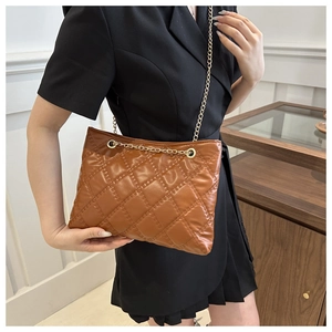 Detail view of brown quilted tote with gold chain strap worn by model in soft lighting