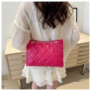 Detail of rose red quilted PU leather tote featuring a gold chain strap on model back