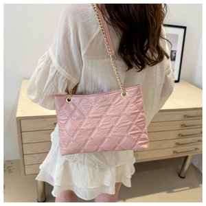 Pink quilted shoulder bag with gold chain strap shown on a model in a cozy room