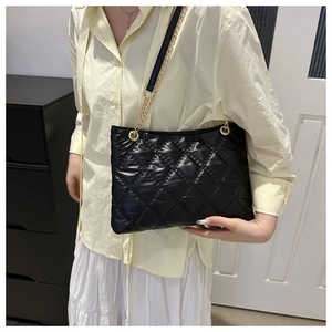 Model wearing a large black quilted tote bag with gold chain strap in a lifestyle setting