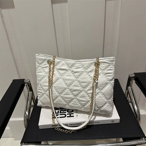 White quilted tote bag with golden chain strap on modern black leather chair background