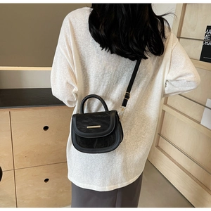 Model wearing black pleated leather saddle bag with gold metal trim in casual indoor setting