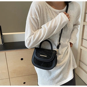 Close-up of a black textured saddle bag with gold metal trim worn on a model's shoulder