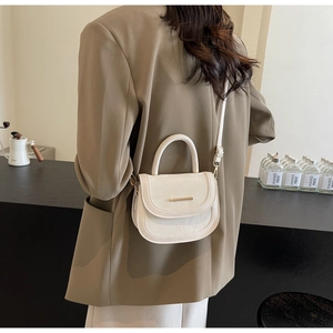 Detail of cream mini saddle bag with gold metal buckle and top handle on casual outfit