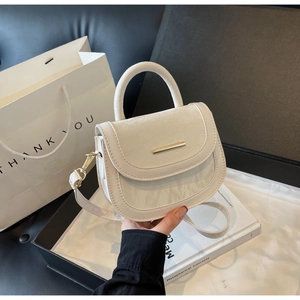 Detail view of cream white saddle bag with fine texture and gold metal buckle hardware