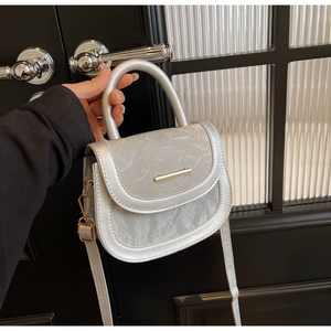 Close-up of pearl silver saddle bag featuring marble texture flap and gold bar buckle detail