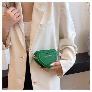 Mini green heart-shaped crossbody bag with silver chain strap shown on a white blazer
