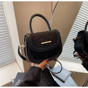 Close-up of black PU and suede saddle bag with gold hardware and a cylindrical handle