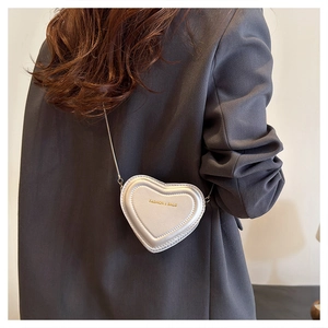 Detail of silver heart-shaped mini crossbody bag with gold lettering and chain strap