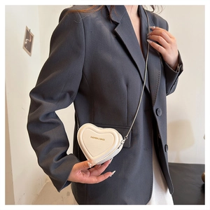 Detail of white heart-shaped crossbody bag with gold embossed lettering and silver chain