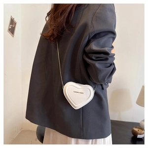 Detail of a white heart-shaped mini crossbody bag with metal chain on a female model
