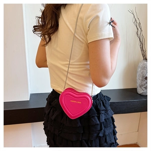Detail of rose red heart-shaped crossbody bag with gold chain strap on female model
