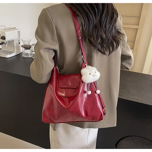 Detail of dark red tote bag with bow accent and white plush cloud charm on a model