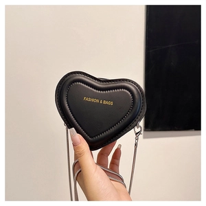 Detail of a black heart-shaped mini bag with gold text and a silver chain strap