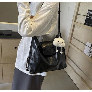 Detailed shot of black patent leather shoulder bag featuring a white cloud plush charm
